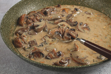 Creamy mushroom sauce simmering in a skillet with sliced mushrooms and herbs on a gray countertop