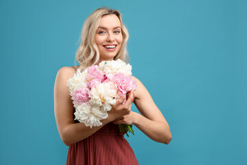 Happy woman with bouquet of beautiful peonies on light blue background