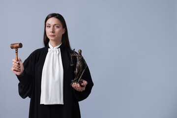 Judge with mallet and figure of Lady Justice on gray background, space for text