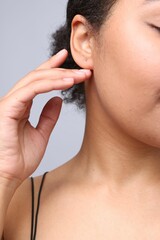 Young woman with pierced ear on light grey background, closeup
