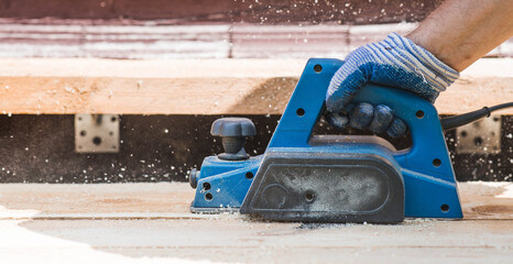 A hand-held electric planer in the hands of a craftsman. A man planing boards with an electric...