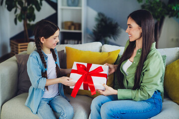 Mother and daughter sharing a special moment at home exchanging a gift while sitting on a cozy sofa...