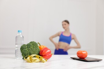 Slim woman posing indoors, focus on vegetables, measuring tape, water and kitchen scale
