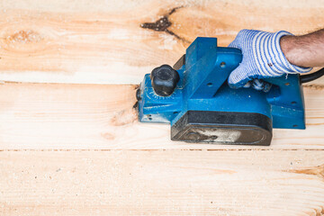 A hand-held electric planer in the hands of a craftsman. A man planing boards with an electric...