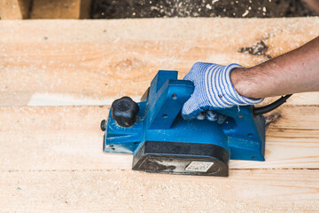 A hand-held electric planer in the hands of a craftsman. A man planing boards with an electric...