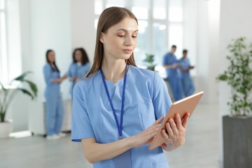 Medical student in uniform with tablet indoors, selective focus