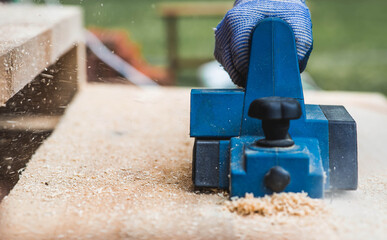 A hand-held electric planer in the hands of a craftsman. A man planing boards with an electric...