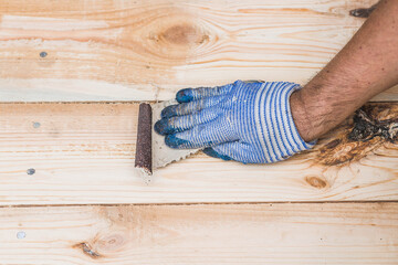 A carpenter wearing cloth gloves manually polishes wooden boards with sandpaper for grinding. The...