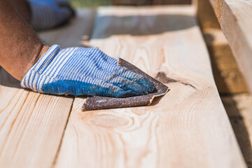 A carpenter wearing cloth gloves manually polishes wooden boards with sandpaper for grinding. The...
