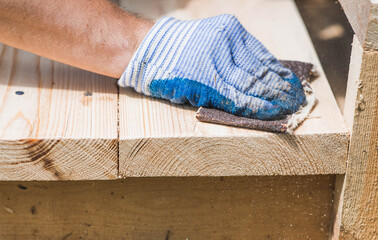 A carpenter wearing cloth gloves manually polishes wooden boards with sandpaper for grinding. The...