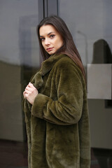 Young woman in faux fur coat. A woman stands near the house on the street.