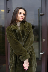 Young woman in faux fur coat. A woman stands near the house on the street.