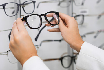 Close-up of hands of a young woman who chooses eyeglasses on the showcase for purchase in an optical store. Optometry, eyesight, glasses, accessories, fashion, lifestyle