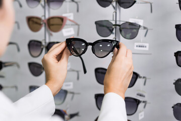 Close-up of hands of a young woman who chooses sunglasses on the showcase for purchase in an optical store. Optometry, eyesight, eyeglasses, accessories, fashion, lifestyle