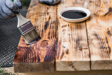 The procedure for protecting and coating wooden boards. A worker applies a protective wood stain with a brush. The process of restoring a hardwood flooring.
