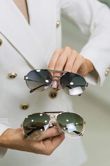 Close-up of the hands of an elegant young brunette woman who holds sunglasses in an optical store. Choosing eyeglasses to buy, vision, protection, lifestyle, fashion