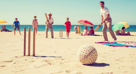 Relaxed beach cricket scene featuring family playing on a sunny day, with ocean backdrop and vintage feel