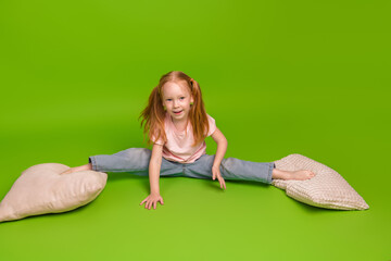 Playful young girl smiling in a casual outfit exploring flexibility in a bright studio with a green...