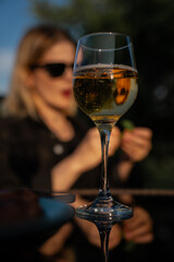 Chilled white wine or sparkling cider in elegant wine glass on reflective table with woman in...