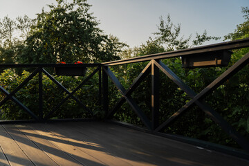 Obraz premium Wooden terrace with decorative railing and garden view, outdoor patio architecture with wooden flooring, greenery, and sunlight shadows for home and landscaping design inspiration