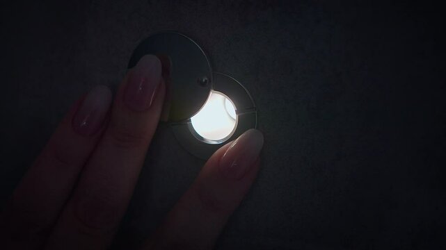 Close-up of a door peephole, a woman's fingers are pushing back the flap