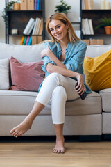 Obraz premium Beautiful young woman posing at camera while holding her mobile phone sitting on couch at home