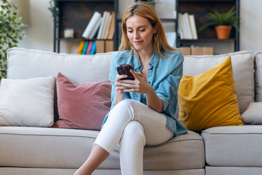 Beautiful young woman using her mobile phone sitting on couch at home