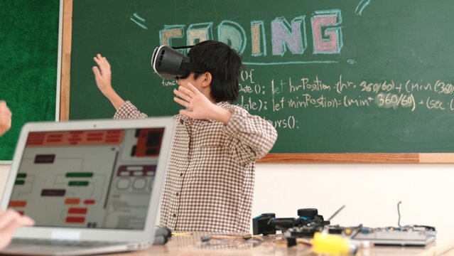 Asian boy wearing VR headset to enter metaworld with electronic board while girl coding system. Group of diverse student working together to develop program and writing engineering code. Pedagogy.