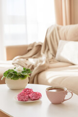 Pink flower marshmallows and tea on a coffee table with a cozy couch. Soft focus
