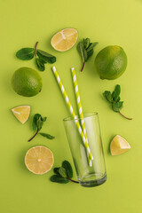 Preparing lemonade. Limes, mint leaves, straws, and a glass on a vibrant green background.