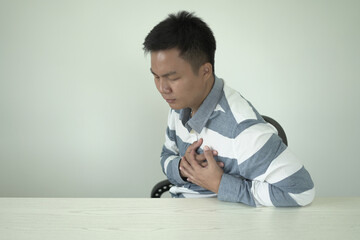 An asian young man who is wearing office outfit is holding his pain area and standing and suffering...