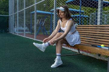 Woman tying shoes on a bench in sportswear on a tennis court