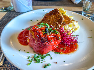Stuffed Spicy Bell Peppers Rocoto Relleno, salsa, garnish, potato gratin in white plate in restaurant. Colorful Traditional Peruvian Food. high angle view, close up