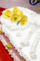 White heart shaped birthday cake. Decorated with yellow flowers and white whipped cream with the inscription Happy Birthday
