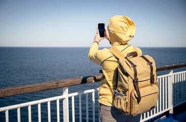 Traveler in yellow jacket taking photo of sea view from ferry deck on sunny day