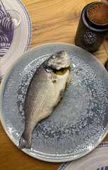 Whole baked sea bass on a plate served for a homemade dinner. Fresh herbs and side garnish create a...