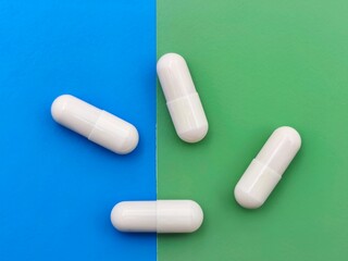 Top view of white capsules placed on a vibrant split-color background of blue and green, illustrating modern pharmaceutical or supplement concepts.
