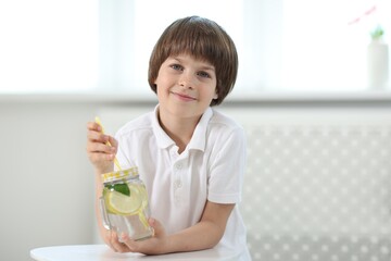Cute little boy with mason jar of lemonade at table indoors. Refreshing drink