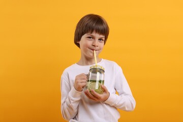 Cute little boy drinking lemonade on orange background. Refreshing drink