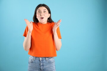 Portrait of surprised woman on light blue background, space for text