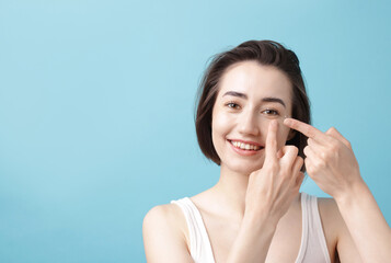 Fototapeta premium Woman putting in contact lens on light blue background. Space for text