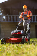 Gardener mowing the lawn in front of a wooden house during a sunny day