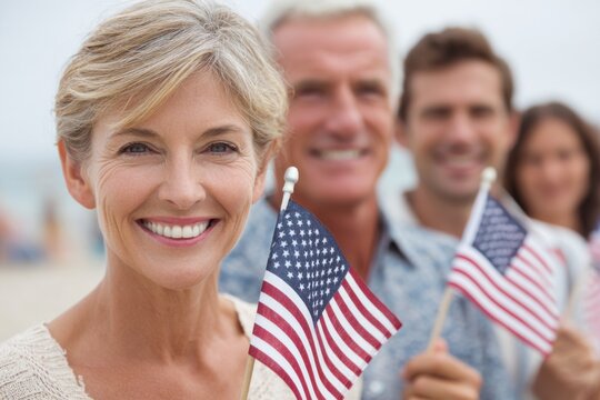 Smiling woman holding small American flag stands in front of friends celebrating national pride at beach, showcasing joy and unity in a festive atmosphere