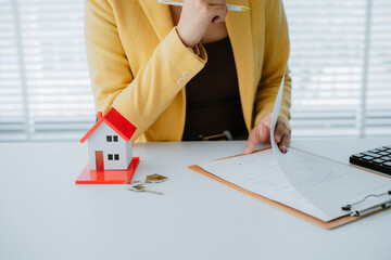 Smiling real estate agent calculating mortgage and presenting house model while sitting at her desk...