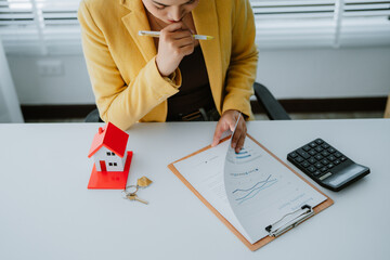 Smiling real estate agent calculating mortgage and presenting house model while sitting at her desk...