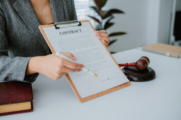 Lawyers discuss a contract on a clipboard, with one pointing to specific terms with a pen, while a...