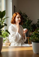 Portrait of a young woman with glowing skin applying moisturizer cream under her eyes.