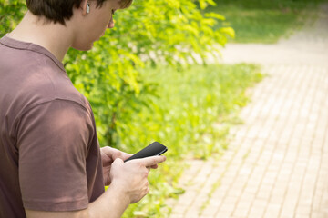 Close up of mans hands holding smartphone in outdoor green setting. Check apps, focused on device,...