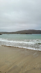 Vertical Beach View with Foamy Waves and Distant Rocky Hills in Ireland