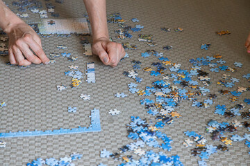 Hands of a person doing on a large jigsaw puzzle on a carpeted floor at home during daytime,...